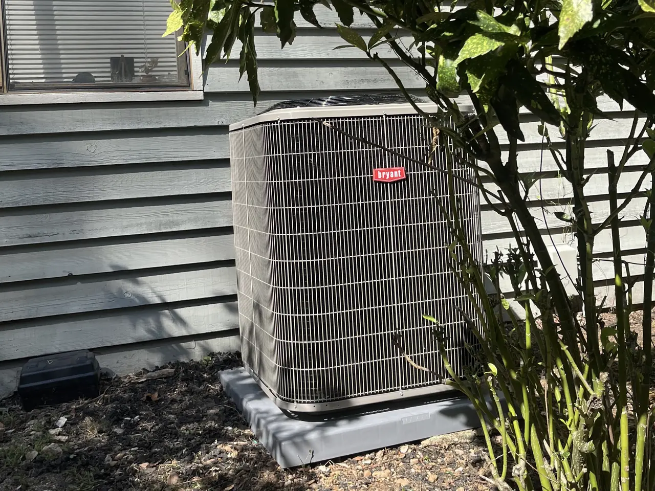 Outdoor HVAC condenser beside gray siding and landscaping